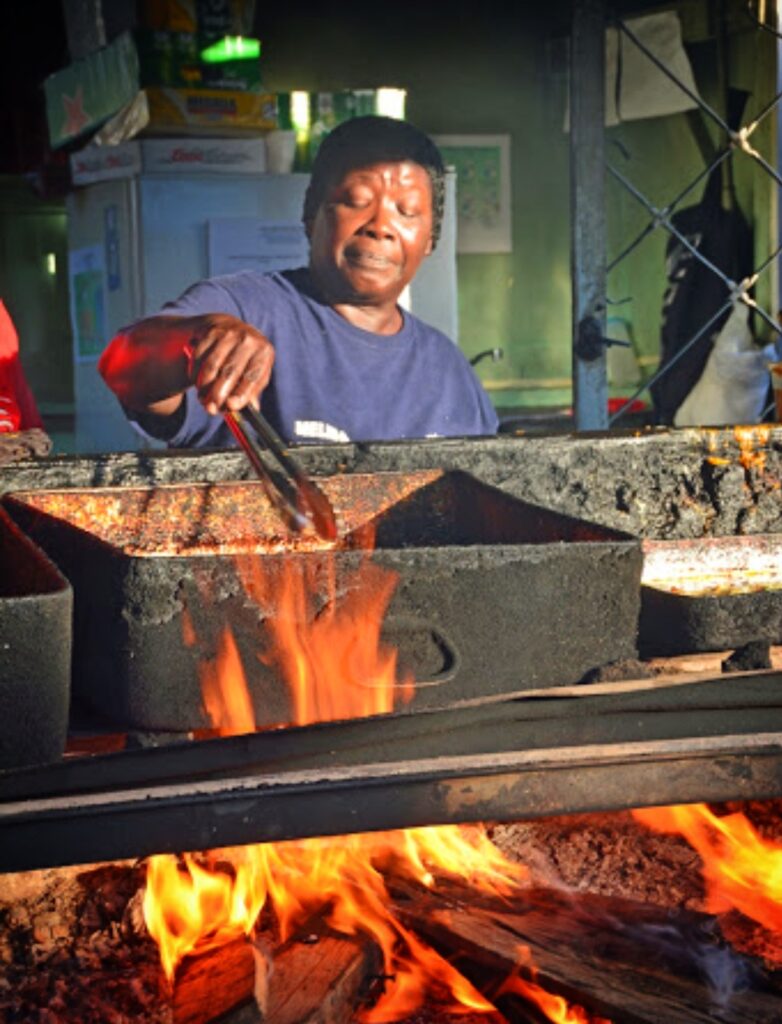 An African American woman from Piñones, Puerto Rico, cooks Authentic African-Taino street food over an open wood flame as part of Bucketlist Tours’ Old San Juan Ageless Elegance, Heritage, and Spirits private tour, celebrating the region’s rich African heritage through history and taste.