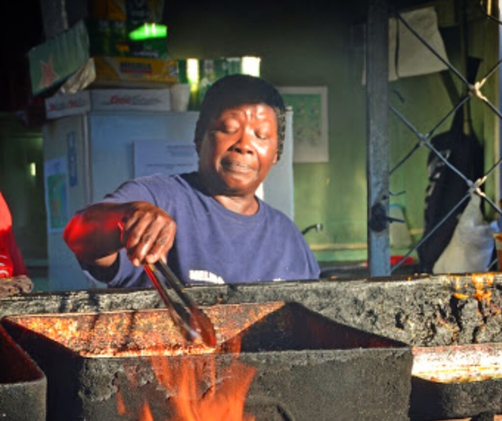 An African American woman from Piñones, Puerto Rico, cooks Authentic African-Taino street food over an open wood flame as part of Bucketlist Tours’ Old San Juan Ageless Elegance, Heritage, and Spirits private tour, celebrating the region’s rich African heritage through history and taste.