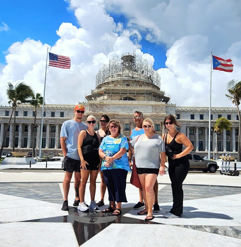 A family with kids and teenagers stands in front of Puerto Rico's State Capitol, a symbol of the island’s transformation from Spanish rule to U.S. Commonwealth status. This educational stop is part of Bucketlist Tours’ Colonial Wonders and Serene Rainforest private Old San Juan tour, which includes over 90 historic landmarks and immersive cultural experiences.