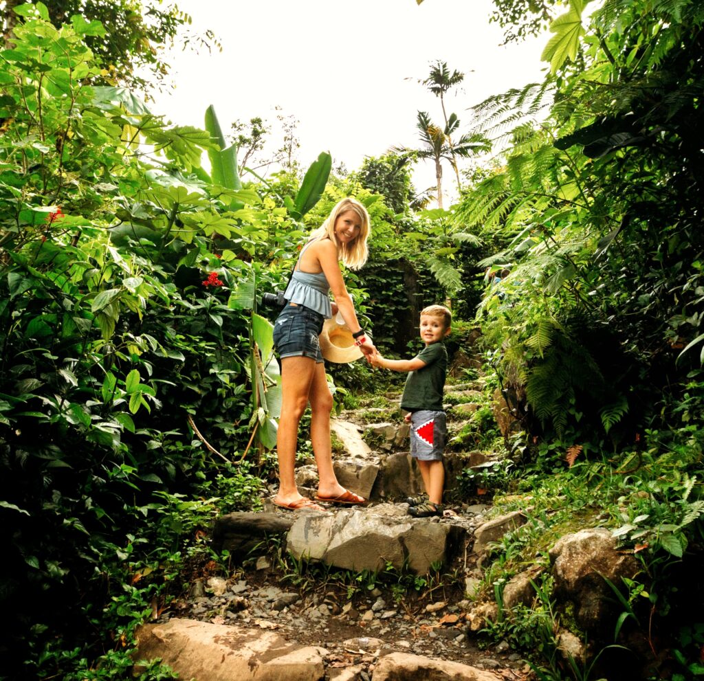 A young mother with her toddler son walks along the easy Angelito Trail in El Yunque Rainforest. She shares the importance of nature and the rainforest with him as he explores the vibrant surroundings with curiosity. This memorable experience is included in Bucketlist Tours’ Colonial Wonders and Serene Rainforest private Old San Juan tour.