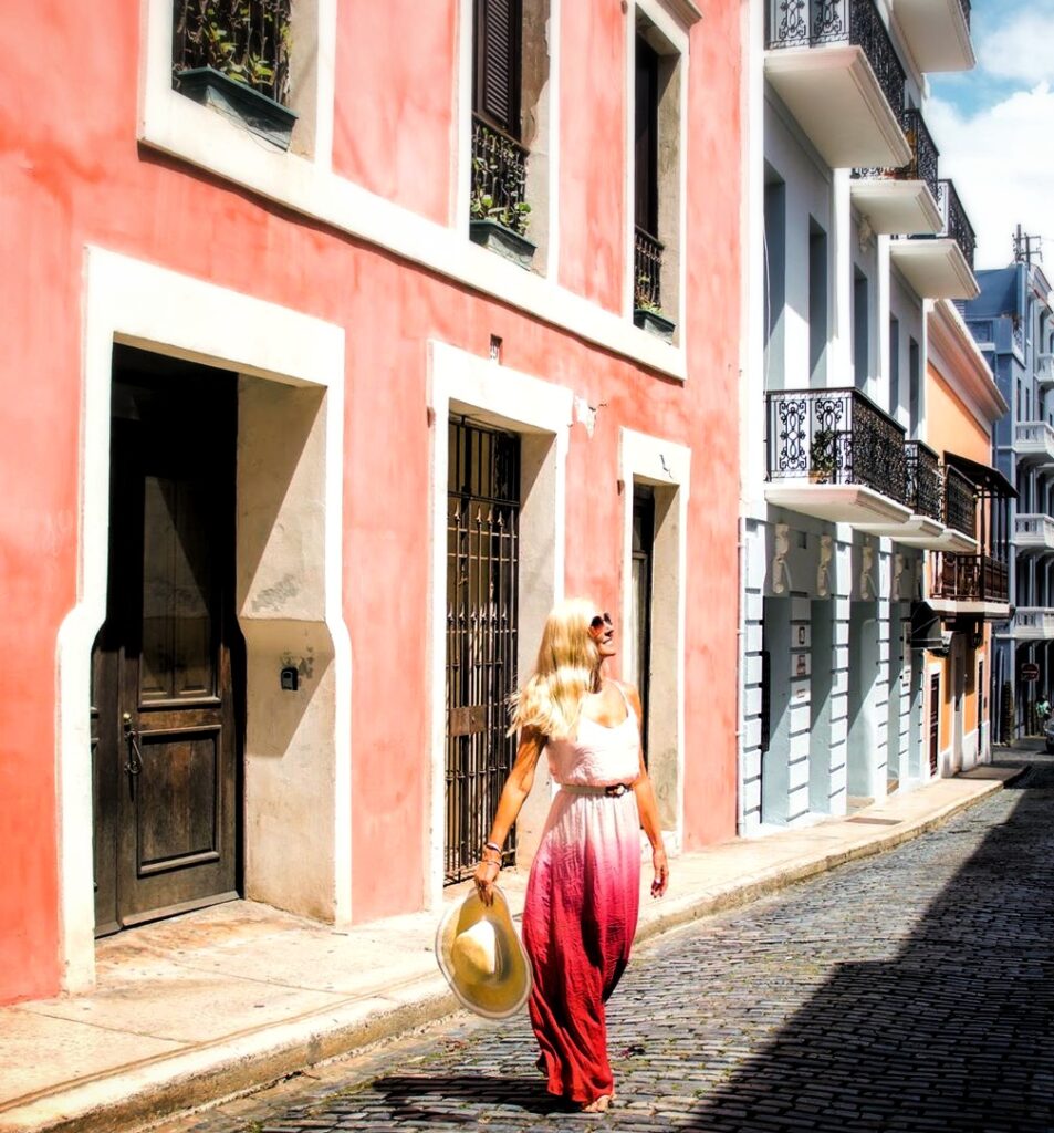 A newlywed, dressed elegantly in a flowing ombré dress, walks through the charming cobblestone streets of Old San Juan. The pastel-colored colonial buildings with wrought-iron balconies line the narrow street, capturing the historic essence of the city. This peaceful and romantic moment is part of Bucketlist Tours’ Colonial Spaniard Splendor and African Spirit Private Old San Juan Tour, designed for safe, comfortable, and memorable exploration.