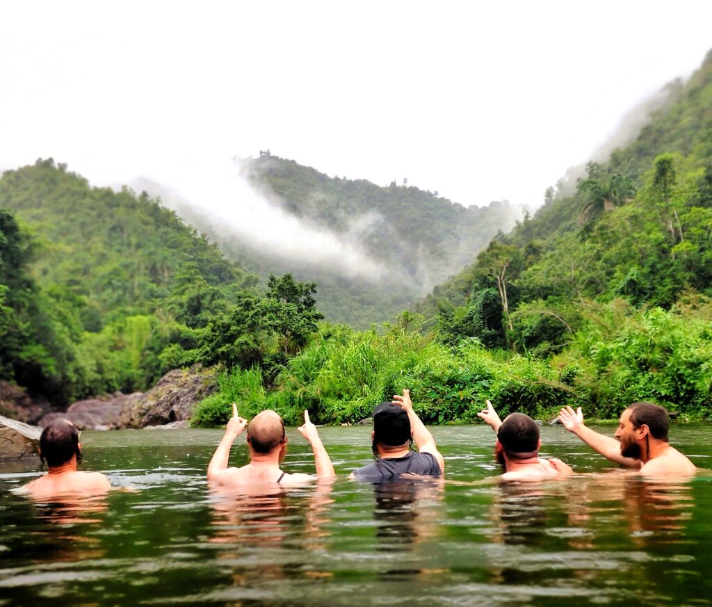 A group of bachelors staying at the Ritz Carlton Reserve at Dorado Beach pose in awe for their guide and ambassador while pointing towards the mist-covered mountains of Toro Negro. This serene moment captures the breathtaking beauty of their first stop during the Tropical Rainforest Magic & Wonders full-day experience by Bucketlist Tours.