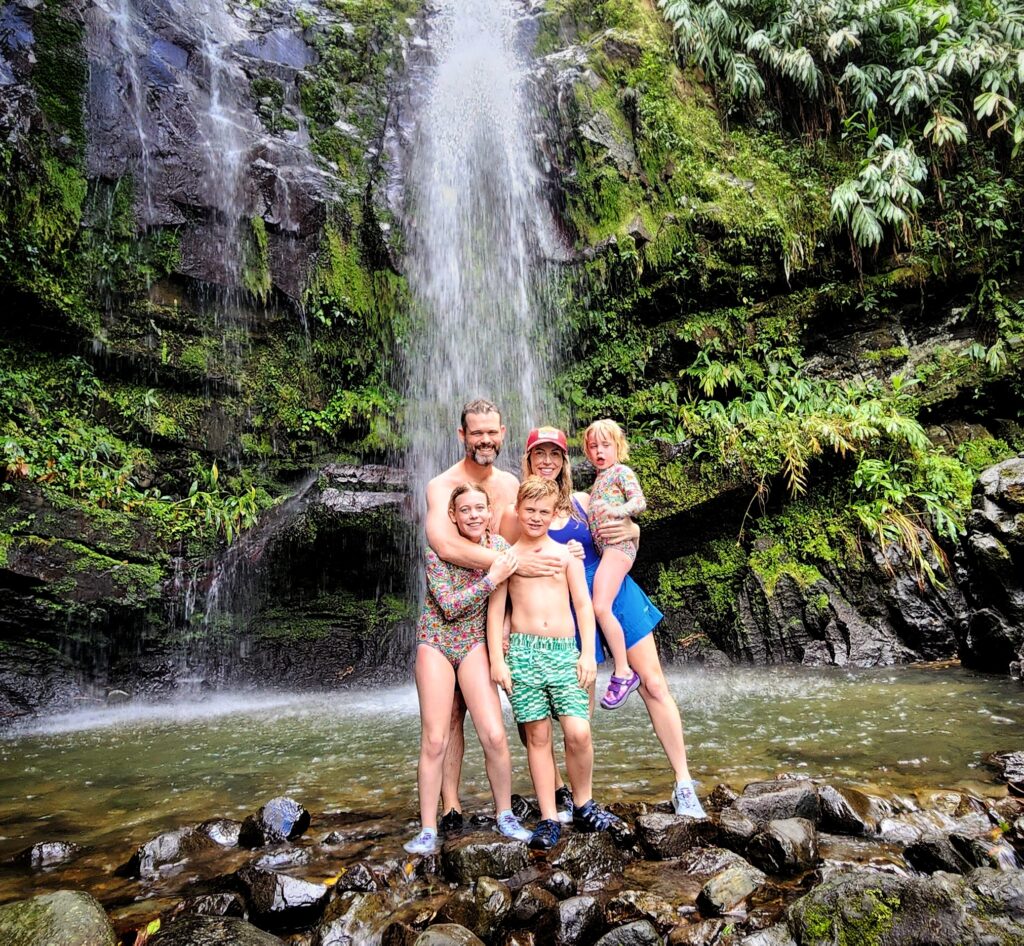 A family of five, including children and toddlers, staying at the luxurious Paradise Villas at Ritz Carlton Reserve in Dorado Beach, joyfully pose with their guide and ambassador in front of Toro Negro's stunning Las Delicias Waterfalls. This serene moment captures the beauty and excitement of their Tropical Rainforest Magic & Wonders full-day experience by Bucketlist Tours.