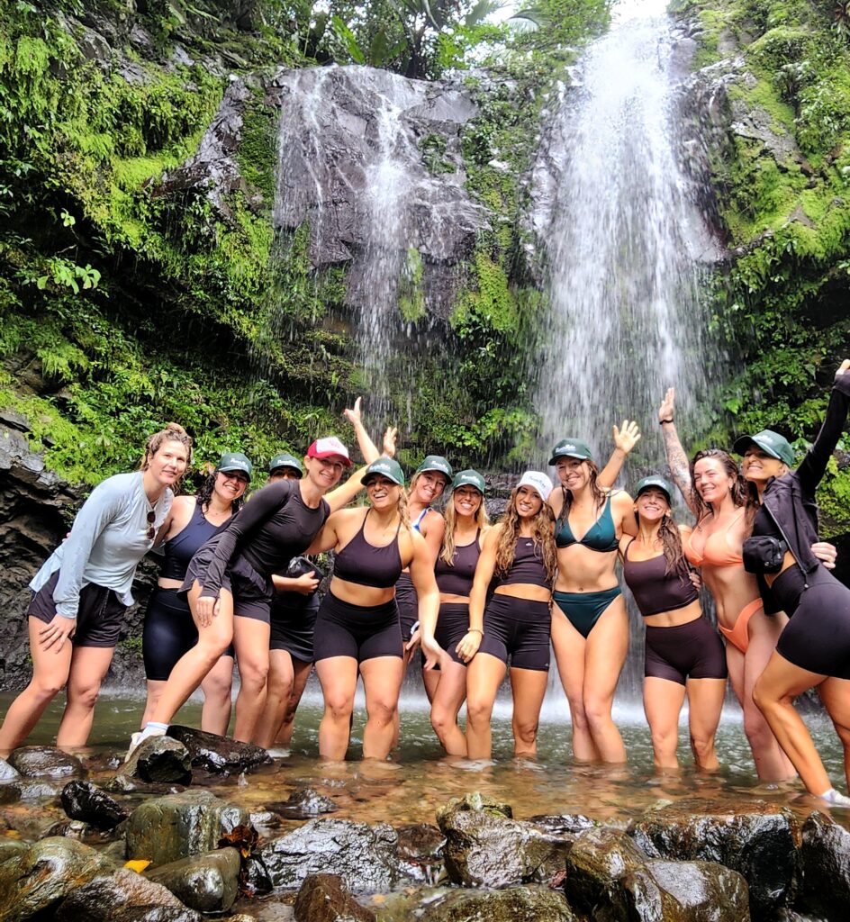 A group of doctors celebrating a bachelorette party, staying at Condado Beach Club, joyfully pose for their guide and ambassador in front of Toro Negro's stunning Las Delicias Waterfalls. This serene and fun-filled moment showcases the beauty and excitement of their Tropical Rainforest Magic & Wonders full-day experience by Bucketlist Tours.