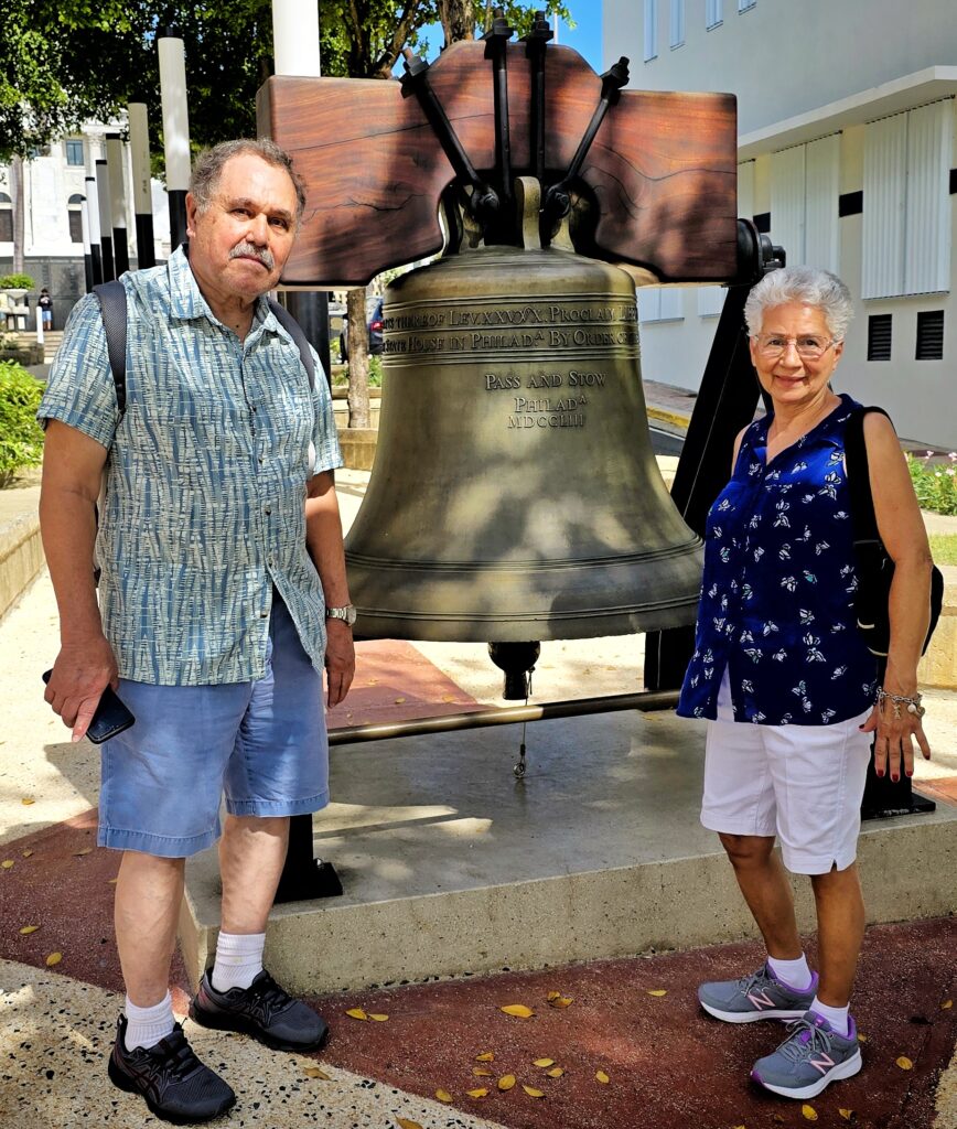 A senior couple traveling to *Puerto Rico* and staying at the Condado Vanderbilt Hotel is captured by their guide and ambassador beside *Puerto Rico’s Liberty Bell*, one of 53 replicas made after World War II to promote *liberty bonds*. The couple learns about the island’s fascinating colonial and *American history*, gaining insights into its unique heritage as part of their Timeless Echoes and Legendary Spirits Old San Juan and *Barrilito Distillery Private Tour*, and just hours to embark in well deserved *Celebrity Cruises* Caribbean Cruise. This one-of-a-kind experience blends a historic Old San Juan tour with a visit to the iconic Barrilito Rum Distillery. The tour covers the entire San Juan Islet and highlights more than 90 landmarks, including the Capitol Building, the Walkway of the Presidents honoring U.S. presidents who have visited Puerto Rico, the North Wall, and the vibrant streets of the old city. Thoughtfully curated with safety and comfort in mind, this tour is ideal for couples, families with children, seniors, and individuals with mobility constraints. Cruise ship passengers can also enjoy this immersive exploration of Old San Juan’s history and distillery heritage.