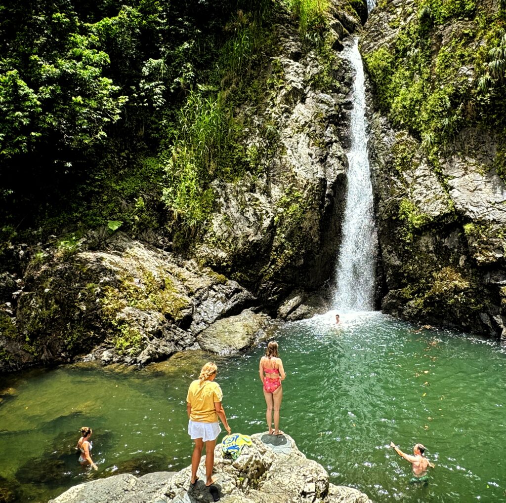 A family with kids and teenagers from Scottsdale, Arizona, staying at the luxurious Condado Vanderbilt Hotel, enjoys a refreshing swim in the tranquil pond beneath the *Chorro de Doña Juana* waterfall in *Toro Negro* Rainforest. This idyllic moment was captured by their guide and ambassador as they enjoyed their Bucketlist Tours' Tropical Rainforest Magic & Wonders. This experience combine a *roadtrip* with magnificent panoramic views, a *rainforest tour*, a visit to a pond with ancient *Taino petroglyphs* and Puerto Rico's finest *waterfalls*; and was part of their Discover Puerto Rico 3 Day package. The only of its kind, offering an exclusive and unique package delivering the top 10 items of any Puerto Rico Vacation Bucketlist offered offered from San Juan, Dorado, Rio Grande, Isabela and Ponce.