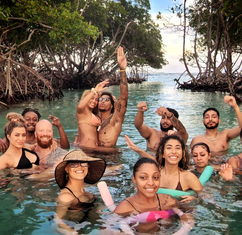 A joyful bridal party, with the newlyweds at the center, poses in the warm, crystal-clear waters of La Parguera's mangrove channels during their Mystic Waters under the Sun & Stars private boat tour. Before heading to the bioluminescent bay, the group enjoyed learning about the ecosystem, conservation efforts, and the science behind the glowing waters. Their adventure concluded with an enchanting swim in the glowing bay under the watchful eye of their guide and ambassador, ensuring a safe and unforgettable experience.