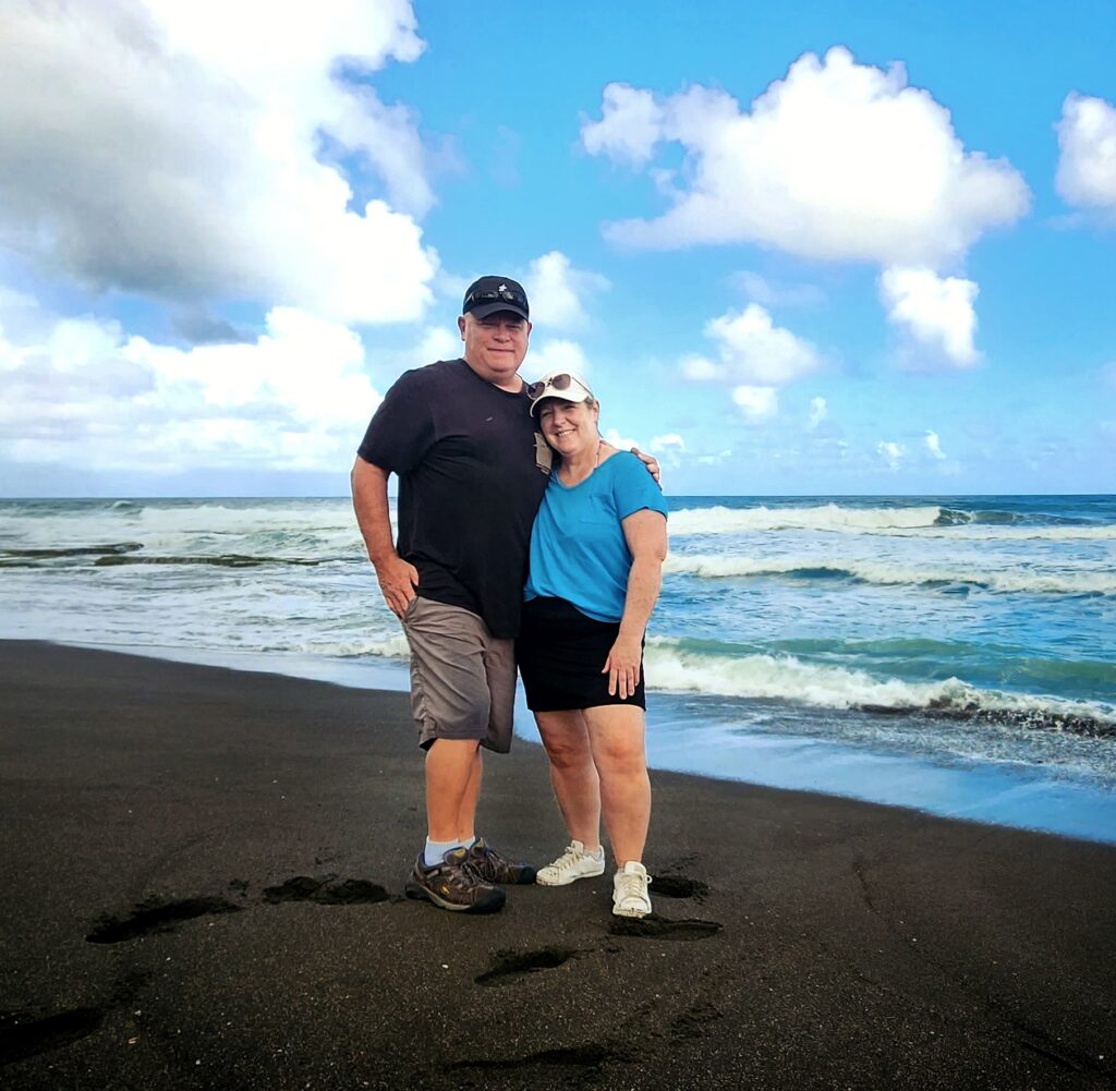 A senior couple from Minnesota, staying at Paradise Villas at the Ritz Carlton Resort in Dorado, joyfully poses with their guide and ambassador at La Boca, one of Puerto Rico's rare black sand beaches. Set against a sunny backdrop with gentle waves lapping at the shore, this scenic stop was part of Bucketlist Tours’ Perfect Beach Escapade: Northern Coastal Adventure Private Experience.