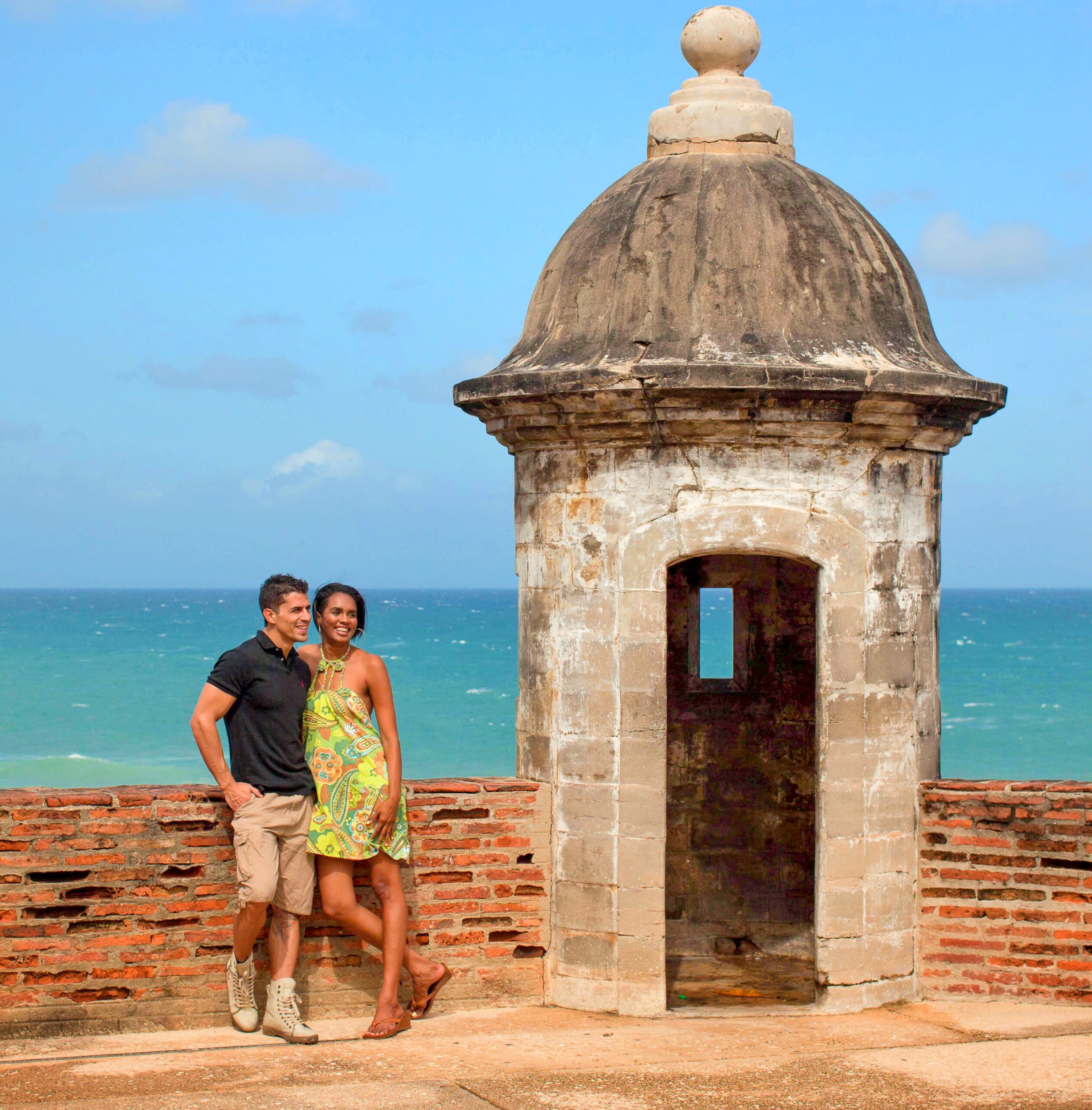 A young couple, staying at the *Condado Vanderbilt Hotel*, poses by a historic garita overlooking the ocean as part of their Old San Juan's Whispers of Time private tour. This exclusive experience allows them to explore the northern walls of *Old San Juan* and learn about its rich colonial history. The most informative and history-packed *Old San Juan tour*, it takes participants through the entire San Juan Islet, visiting over 90 landmarks, including the Capitol Building, the *Walkway of the Presidents* (honoring U.S. presidents who visited *Puerto Rico* while in office), the iconic north wall, and the main streets of the old city. The tour offers three lengths: a 2-hour comfortable *sightseeing tour* in a luxury air-conditioned vehicle, a 3-hour version with 2–3 stops for photos and exploration, and a 4-hour option featuring 4 extended stops. Curated with safety and comfort in mind, this experience is perfect for families with children, seniors, or those with mobility constraints, ensuring a stress-free and enriching journey.