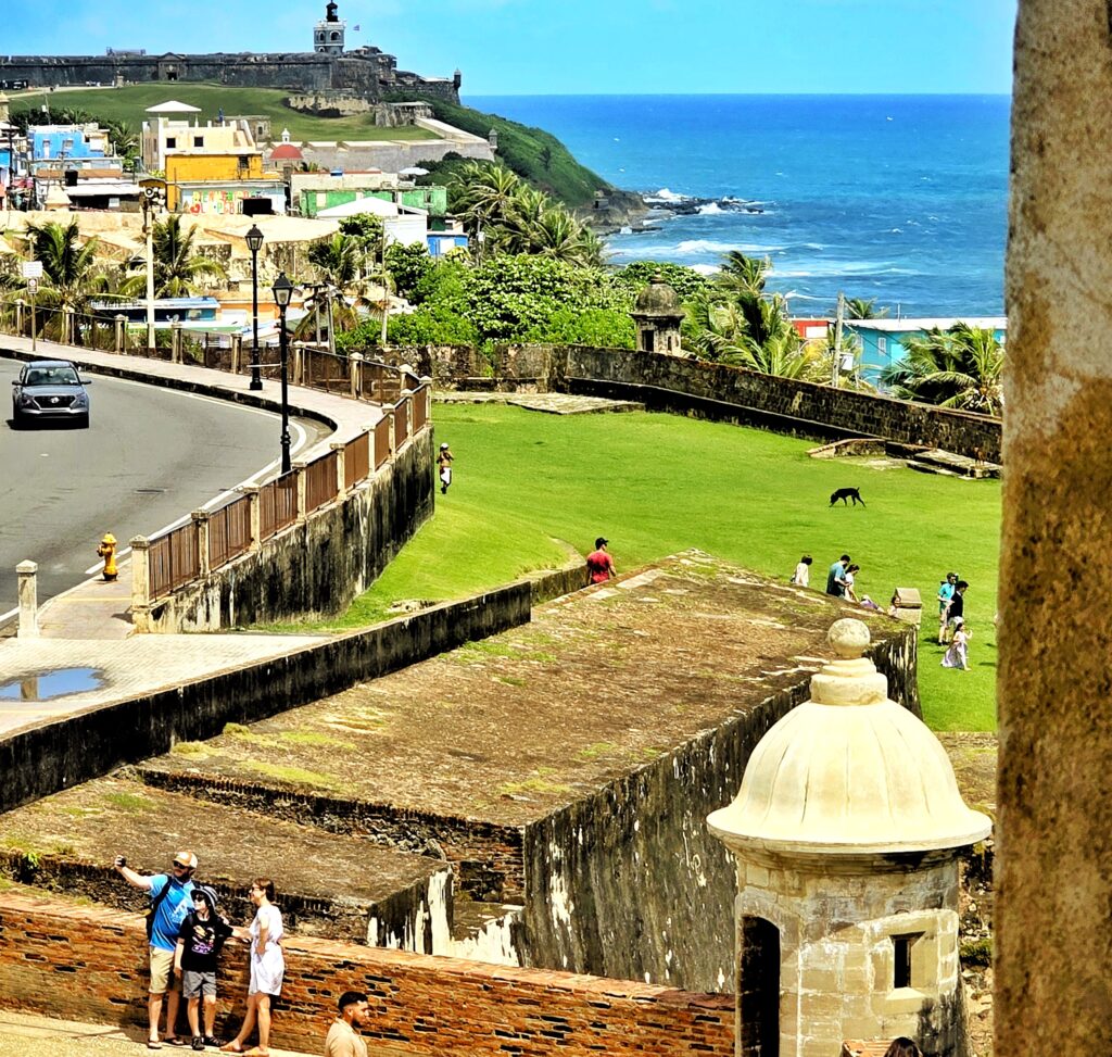 A family of three, traveling aboard the *Ritz Carlton Cruise* Ship *Evrima*, is captured in a panoramic image of Old San Juan’s iconic north wall. Their guide and ambassador immortalizes the moment as the family takes a selfie against the backdrop of the vibrant northern fortifications. While enjoying this scenic view, they learn about Puerto Rico's critical military history, including its strategic role in the Allied victory during World War II against Nazi Germany and Japan. This is part of their Old San Juan's Whispers of Time private tour, renowned for being the most informative and history-packed exploration of *Old San Juan*. Covering over 90 landmarks across the San Juan islet, including the Capitol Building, the *Walkway of the Presidents*, and the picturesque main streets. The tour is the perfect *shoreline excursion* for cruiseship passengers being offered in three flexible durations: 2 hours for a sightseeing journey in a luxury air-conditioned vehicle, 3 hours with 2–3 photo stops, or 4 hours with 4 extended exploration stops. Designed with safety and comfort in mind, this *Old San Juan tour* is ideal for couples, families with children, seniors, or anyone seeking a leisurely yet enriching adventure.