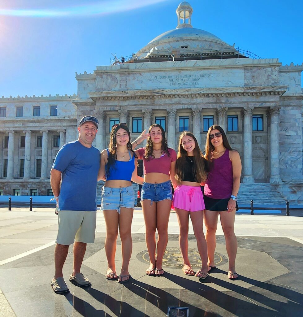 A family of five traveling to Puerto Rico aboard a *Royal Caribbean* Cruiseship is captured by their guide and ambassador as they pose in front of the iconic *State Capitol building*. This sunny moment highlights their discovery of Puerto Rico's extraordinary contributions to America's military efforts—from World War I to the Korean and Vietnam Wars, World War II, and the ongoing War on Terror. They also learned about Puerto Rico’s significant transformation after becoming a Commonwealth of the United States. This enriching experience is part of their Old San Juan's Whispers of Time private tour, the most comprehensive and history-rich exploration of *Old San Juan*. Spanning the entire *San Juan Islet*, the tour features over 90 landmarks, including the Capitol Building, the *Walkway of the Presidents* that honors U.S. presidents who have visited the island, the North Wall, and the charming main streets of the old city. It is the deal *shoreline excursion* for cruise ship passengers, this tour is available in three customizable durations: 2 hours for a comfortable sightseeing overview in a luxury air-conditioned vehicle, 3 hours for exploration with photo stops, and 4 hours for a fully immersive experience with extended stops. Thoughtfully designed for families, couples, seniors, and those seeking a comfortable yet enriching journey, this *Old San Juan tour* ensures unforgettable moments and deep cultural connections.