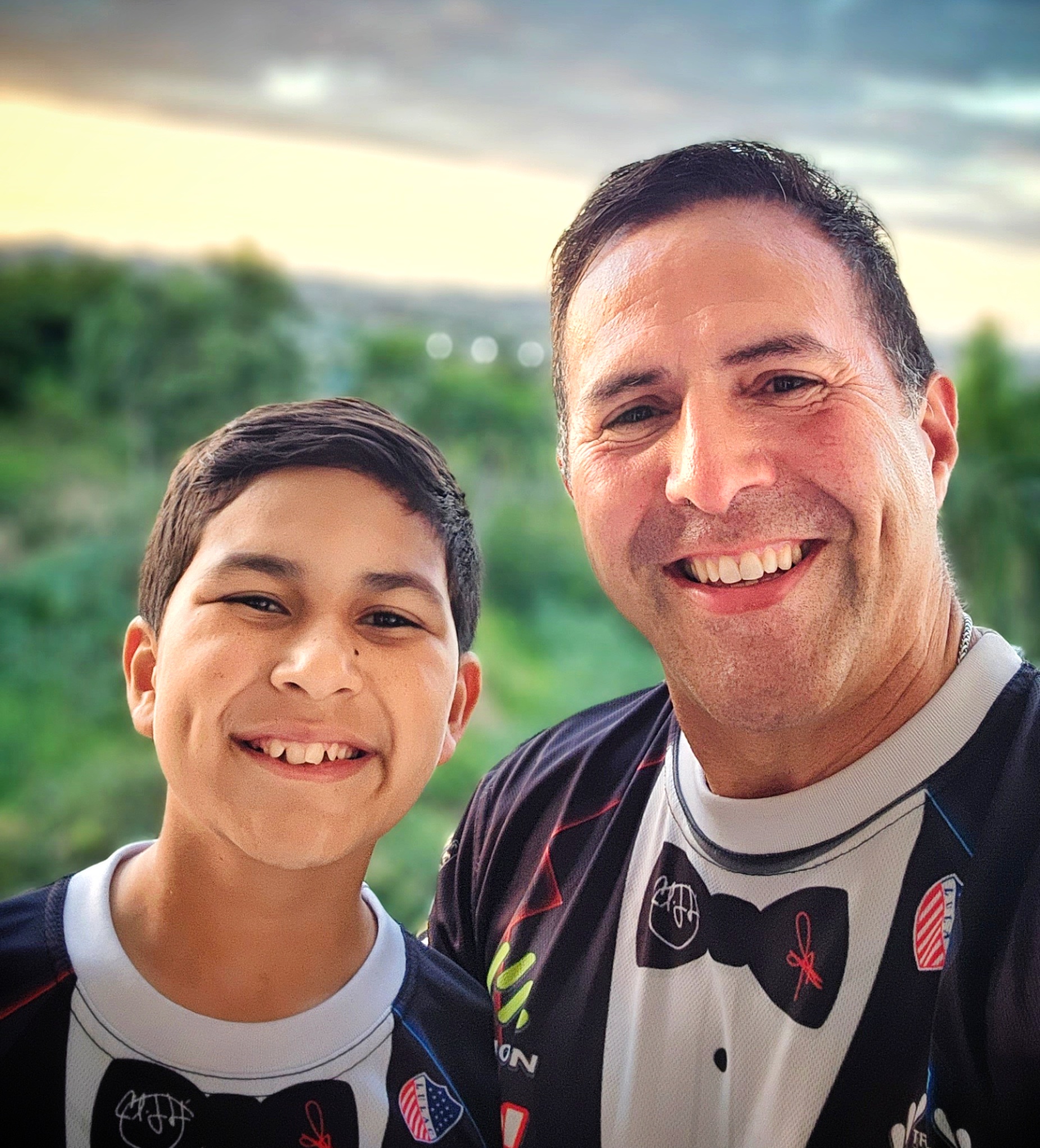 Marcos and Papito!, co-founders of Bucketlist Tours, smile warmly while wearing their signature uniforms, set against the stunning backdrop of a sunset over Puerto Rico's lush tropical rainforest. Their passion and dedication shine as they and their team work tirelessly to answer questions, provide expert guidance, and ensure guests confidently book their dream experiences on the island.